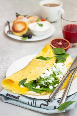 Omlet ıspanak, avokado ve taze çiftlik süzme peynir (tvorog) ve süzme peynirli börek (syrniki) ekşi krema, taze meyveler ve ışık gri arka plan üzerine nane ile servis. Kahvaltı veya diyet sağlıklı öğle yemeği. Kopya alanı.