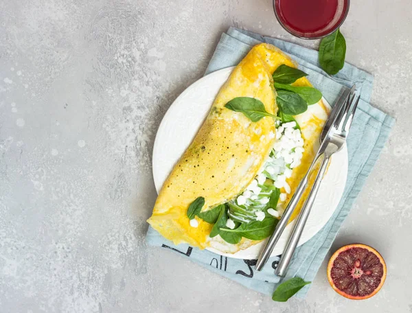 Omelette with spinach, avocado and fresh farm cottage cheese (tvorog) with red orange juice on a light grey background. Healthy breakfast or diet lunch. Copy space.