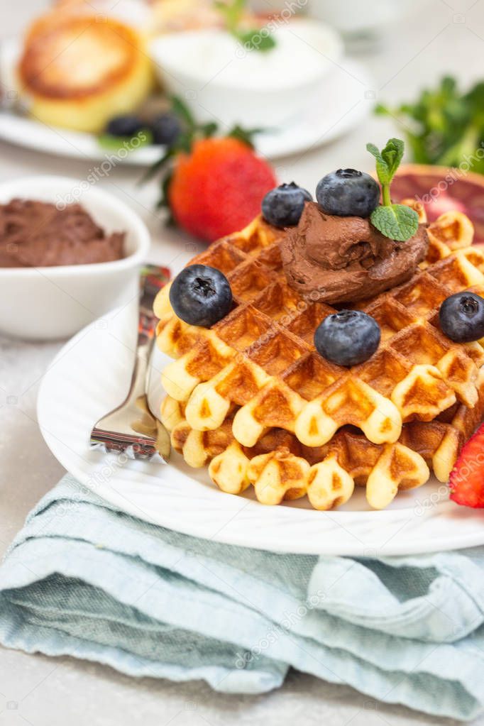 Belgian waffles with chocolate sauce, berries and mint and cottage cheese pancakes on a light gray background. Breakfast or lunch. Copy space.