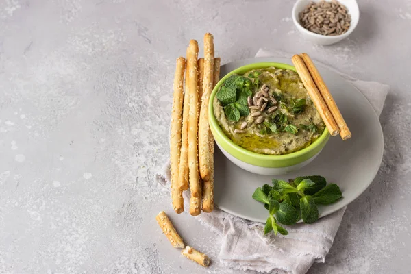 Dip with mung beans, mint and seeds served with grissini or salted bread sticks. Green hummus. Light grey background. Copy space. Healthy snack.