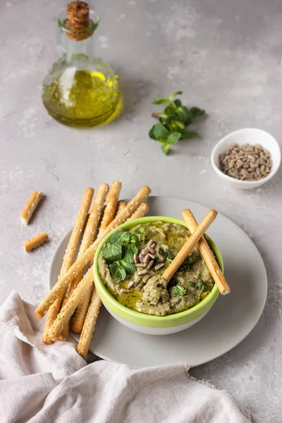 Dip with mung beans, mint and seeds served with grissini or salted bread sticks. Green hummus. Light grey background. Copy space. Healthy snack.