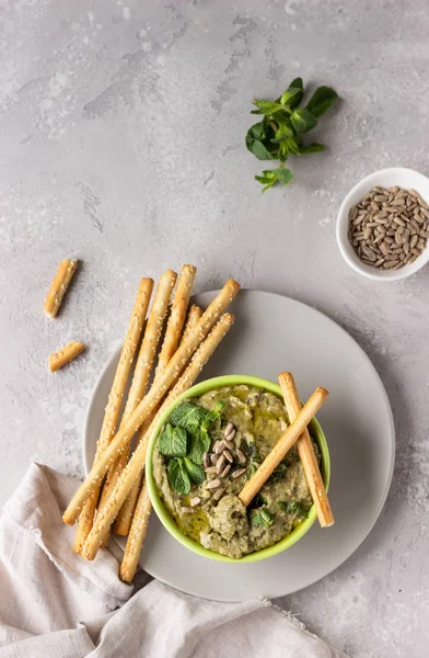 Dip with mung beans, mint and seeds served with grissini or salted bread sticks. Green hummus. Light grey background. Copy space. Healthy snack.