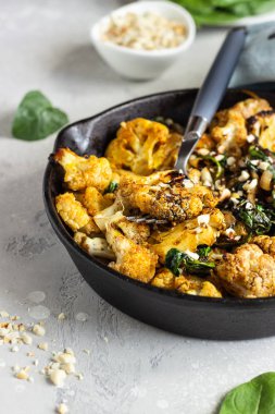 Fırında karnabahar, ıspanak, kuru üzüm ve demir bir tavada fındık. Açık gri arkaplan. Uzayı kopyala Sağlıklı vejetaryen yemekleri.