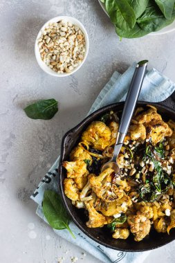 Fırında karnabahar, ıspanak, kuru üzüm ve demir bir tavada fındık. Açık gri arkaplan. Uzayı kopyala Sağlıklı vejetaryen yemekleri.