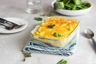 Açık gri arka planda balık ve peynir ile patates güveç.