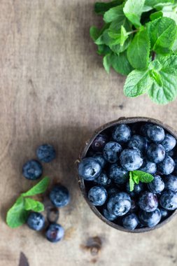 Ahşap kasede taze topalmış yaban mersini. Sulu ve ahşap masada nane ile taze yaban mersini. Rustik arka planda bilberry. Yaban mersini antioksidan. Sağlıklı beslenme ve beslenme kavramı. 