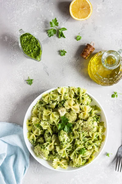 Pasta with green sauce and roaster cauliflower on a white plate. Copy space.