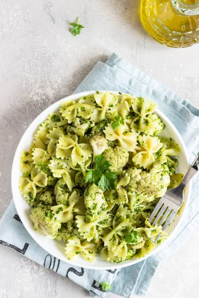 Beyaz bir tabak ta yeşil soslu makarna ve kavurma karnabahar. Kopyalama alanı.