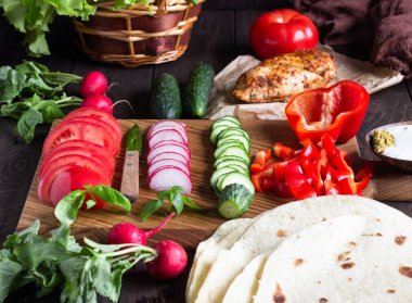 Sarar için Malzemeler: buğday unu tortilla, kavrulmuş tavuk, çeşitli sebzeler, yeşil salata ve ahşap tahta üzerinde sos ile fesleğen.