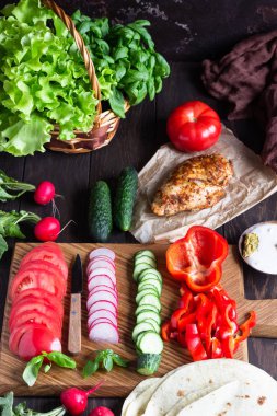 Sarar için Malzemeler: buğday unu tortilla, kavrulmuş tavuk, çeşitli sebzeler, yeşil salata ve ahşap tahta üzerinde sos ile fesleğen.