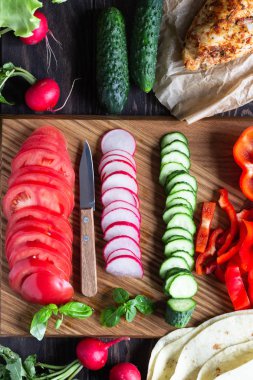 Sarar için Malzemeler: buğday unu tortilla, kavrulmuş tavuk, çeşitli sebzeler, yeşil salata ve ahşap tahta üzerinde sos ile fesleğen.