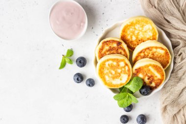 Taze yaban mersini, nane ve sos ile süzme peynir börek (syrniki). Açık gri arka plan. Sağlıklı kahvaltı veya diyet öğle yemeği. Kopyalama alanı.