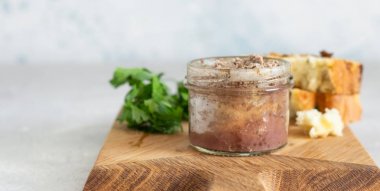 Bir ahşap kesme tahtasında taze ekmek ve maydanoz ile bir cam kavanoz karaciğer pate. Açık gri taş arka plan.