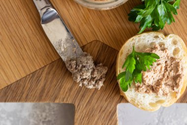 Bir ahşap kesme tahtasında taze ekmek ve maydanoz ile bir cam kavanoz karaciğer pate. Açık gri taş arka plan.