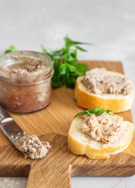 Bir ahşap kesme tahtasında taze ekmek ve maydanoz ile bir cam kavanoz karaciğer pate. Açık gri taş arka plan.