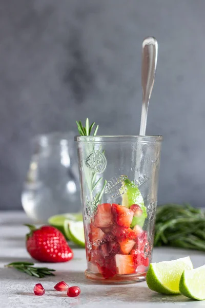 Strawberry lemonade and ingredients (strawberry, pomegranate, rosemary and lime) on light grey background. Copy space.