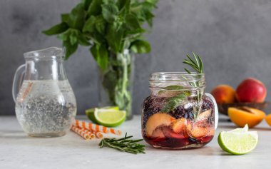 Açık gri taş masa üzerinde taze kayısı, biberiye, nane ve kireç ile cam ev yapımı kayısı ve siyah frenk üzümü limonata. Serinletici yaz içkisi. Kokteyl bar arka plan konsepti. Kopyalama alanı.