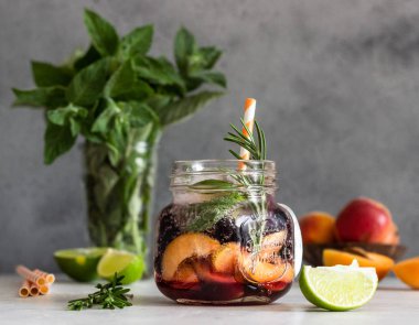 Açık gri taş masa üzerinde taze kayısı, biberiye, nane ve kireç ile cam ev yapımı kayısı ve siyah frenk üzümü limonata. Serinletici yaz içkisi. Kokteyl bar arka plan konsepti. Kopyalama alanı.