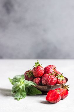 Açık gri taş masada nane ile ahşap bir kapta çilek.