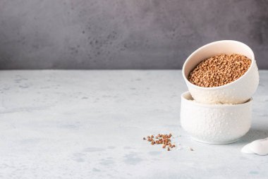 Beyaz kaselerde karabuğday ve pirinç. Sağlıklı kahvaltı. Açık taş arka plan. Kopyalama alanı.