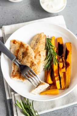 Izgara tavuk veya hindi fileto (biftek), kavrulmuş havuç ve biberiye beyaz bir tabak, gri taş arka plan.