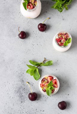 Cam kavanozlarda kiraz, taze kiraz ve gri taş arka planda nane ile pişmiş cheesecake yok. Sağlıklı tatlı. Kopyalama alanı.