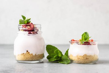 Cam kavanozlarda kiraz, taze kiraz ve gri taş arka planda nane ile pişmiş cheesecake yok. Sağlıklı tatlı. Kopyalama alanı.