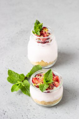 Cam kavanozlarda kiraz, taze kiraz ve gri taş arka planda nane ile pişmiş cheesecake yok. Sağlıklı tatlı. Kopyalama alanı.