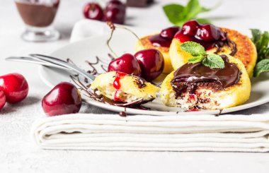 Süzme peynir krep veya çikolata ve vişne reçeli, taze kiraz ve nane ile börek. Geleneksel Ukrayna ve Rus mutfağı. Syrniki, ne oldu? Sağlıklı ve diyet kahvaltı.