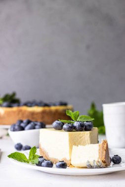 New York tarzı cheesecake, taze yaban mersini ve nane beyaz bir tabak ta. Açık taş arka plan. Kopyalama alanı.
