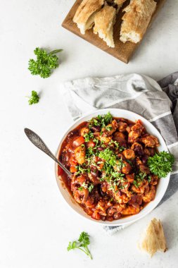 Açık gri kayrak veya taş arka plan üzerinde beyaz bir tabaktabak tabaktabak domates soslu kırmızı fasulye, biber ve soğan ile et güveç. 