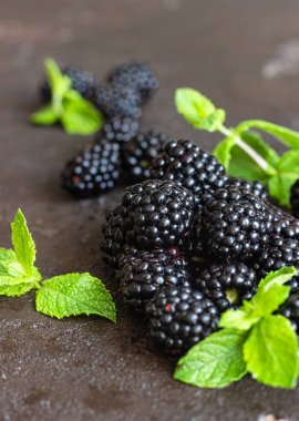 Koyu kahverengi taş arka planda nane yaprakları ile olgun böğürtlen. Seçici odak, kopya alanı.