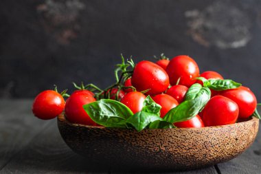 Taze kiraz domates ve fesleğen bir ahşap plaka karanlık bir arka planda. Hasat domates. 