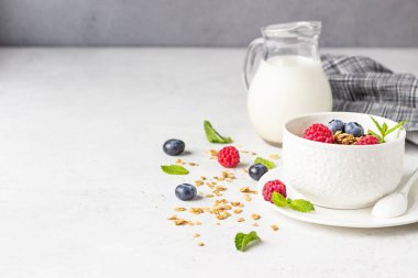 Süt, taze çilek (yaban mersini ve ahududu) ve süt ile ev yapımı granola Beyaz seramik kase. Sağlıklı kahvaltı malzemeleri. 