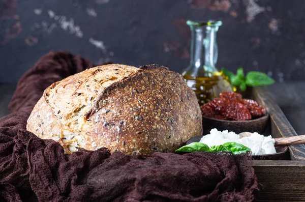 リコッタチーズ ドライトマト バジル オリーブオイルを添えた 裏粉のサワーパンの丸いパン 暗い木製の背景 素朴なスタイル — ストック写真