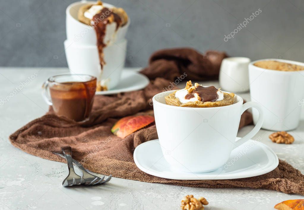Carrot or pumpkin mug cupcake with whipped cream, caramel sauce and walnuts in a white ceramic mug. Cozy autumn or winter breakfast. Healthy dessert. 