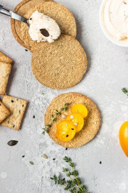 Siyah bir tabak üzerinde krem peynir ve domates ile ince gevrek kepekli kraker. 