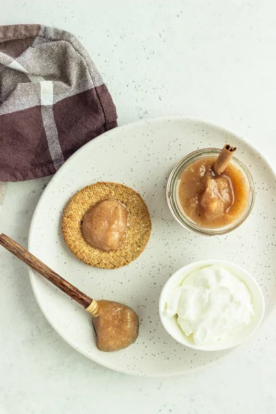 Gri bir tabak üzerinde doğal yoğurt ve reçel ile ince gevrek kepekli kraker. Sade kahvaltı veya atıştırmalık. 