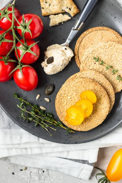 Siyah bir tabak üzerinde krem peynir ve domates ile ince gevrek kepekli kraker. 