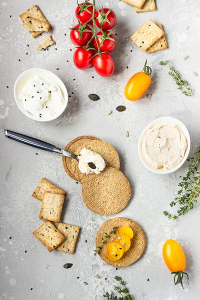 Siyah bir tabak üzerinde krem peynir ve domates ile ince gevrek kepekli kraker. 