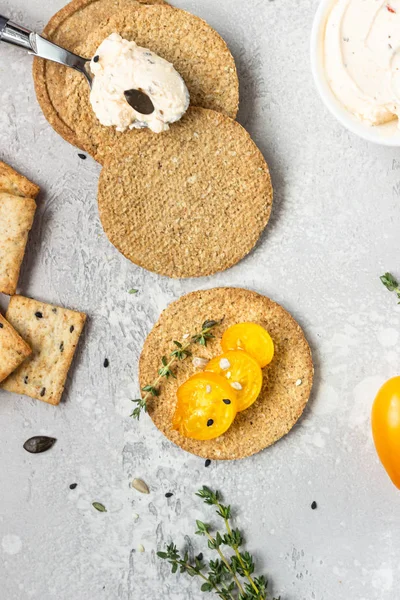 Siyah bir tabak üzerinde krem peynir ve domates ile ince gevrek kepekli kraker. 