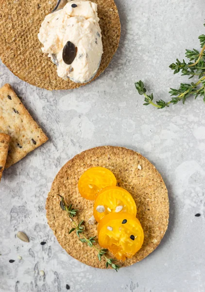 Siyah bir tabak üzerinde krem peynir ve domates ile ince gevrek kepekli kraker. 