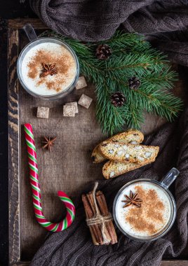 Eggnog. Tarçın ile Noel süt kokteyli, biscotti çerezleri, kış baharat, şeker ve köknar dalı ile ahşap tepsi üzerinde iki cam kupalar servis.