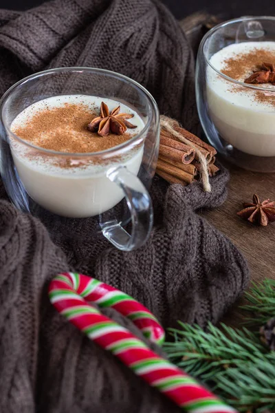 エッグノッグ シナモンとクリスマスミルクカクテル ビスコッティクッキーと木製のトレイに2つのガラスのマグカップで提供 冬のスパイス キャンディーやモミの枝 — ストック写真