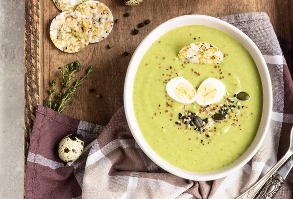 Green broccoli cream soup with quail egg, crackers and seed mix on a wooden tray. Top view. Healthy eating. — Stock Image Green Broccoli Cream Soup Quail Egg Crackers Seed Mix Wooden Royalty Free Stock Images