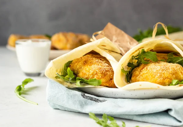 Tortilla wraps with chicken or turkey cutlets, arugula and sour cream sauce on a ceramic plate.