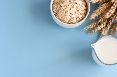 Sütlü yulaf sütü ve yulaf ezmesi beyaz bir seramik kasede mavi kağıt arka planda. Alternatif süt. Vejetaryen süt sütü.