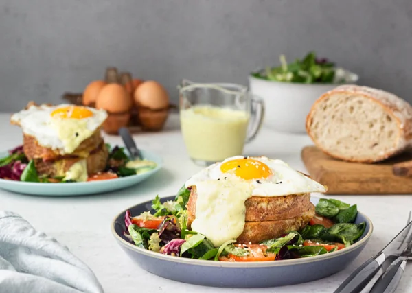 Croque Madame - hot french sandwich with ham, melted emmental cheese, fried egg and bechamel sauce with salad. Delicious breakfast.