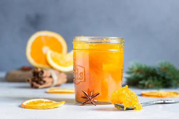 Homemade orange jam with orange peel in a glass jar as a gift for Christmas or New year with fir branches, spices (cinnamon and anise) and orange. Selective focus.