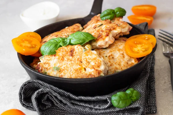 Snijwonden. Gebakken heerlijke kip- of kalkoenkoteletten in gietijzeren pan met basilicum, tomaten en saus. Lichtgrijze stenen achtergrond. — Stockfoto